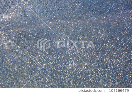broken tempered glass in cracks, spoiled glass surface texture on blue sky background, shine from bright light, close-up. broken tempered glass in cracks, spoiled glass surface texture on blue sky background, shine from bright light, close-up. 105166479