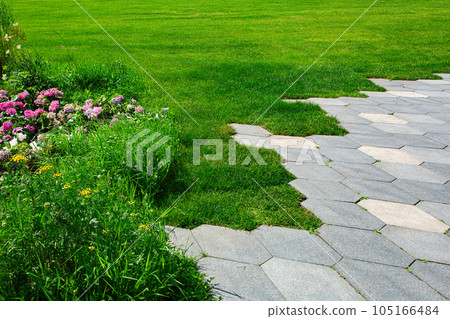 walkway with concrete tiles honeycomb pattern and flowerbed with flowers near green lawn lit by sunlight close-up, nobody. walkway with concrete tiles honeycomb pattern and flowerbed with flowers near green lawn lit by sunlight close-up, nobody. 105166484