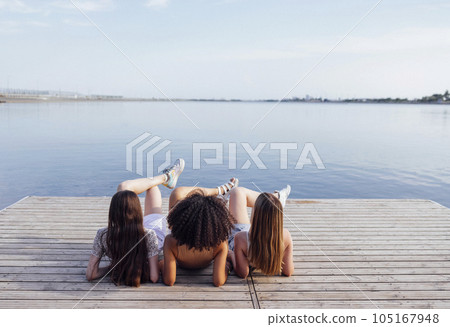 Funny multiracial teenage girls lie on a wooden floor outdoors. 105167948