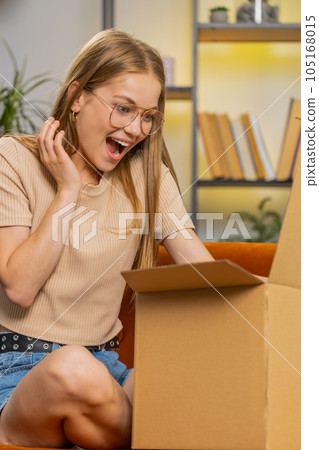 Happy young woman shopper unpacking cardboard box delivery parcel online shopping purchase at home 105168015
