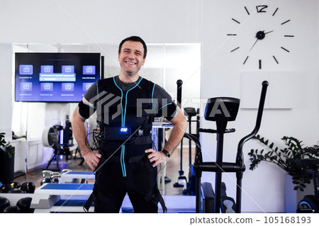 Portrait of satisfied smiling man in special ems suit standing in the middle of the gym or fitness club. 105168193