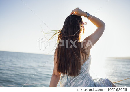 A young woman in a beautiful elegant sundress sits on the deck of a ship and meets the sunrise 105168656
