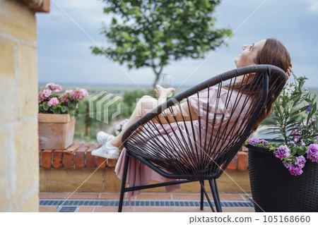 Attractive young woman is sitting on wicker chair in backyard of house. 105168660