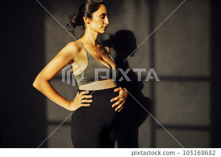 Pregnant woman against a gray texture wall with shadow silhouette Pregnant woman against a gray texture wall with shadow silhouette 105168682