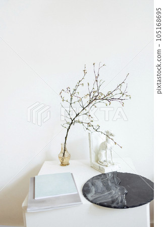 Square white wooden table with acrylic round painting, notebooks, glass transparent vase and tree branch, marble hound dog statue. Square white wooden table with acrylic round painting, notebooks, glass transparent vase and tree branch, marble hound dog statue. 105168695