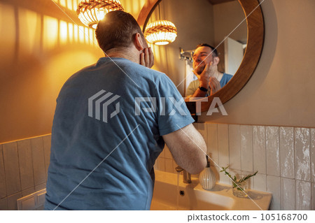 Young attractive man looks out the window and wipes his hands with white towel in his bathroom Young attractive man looks out the window and wipes his hands with white towel in his bathroom 105168700