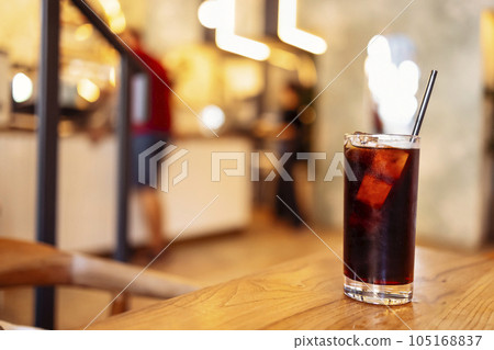Glass of delicious coffee with ice cubes and a straw on a wooden backdrop. Glass of delicious coffee with ice cubes and a straw on a wooden backdrop. 105168837
