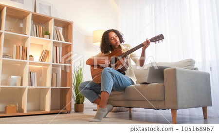 Song learning. Guitar playing. Music hobby. Focused woman musician practicing chords of string acoustic instrument sitting couch at living room. 105168967