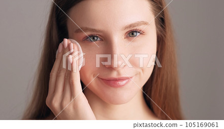 Face cleansing. Morning procedure. Freshness rejuvenation. Pretty smiling woman tenderly touching radiant glowing skin with facial cotton care pad isolated on beige. Face cleansing. Morning procedure. Freshness rejuvenation. Pretty smiling woman tenderly touching radiant glowing skin with facial cotton care pad isolated on beige. 105169061