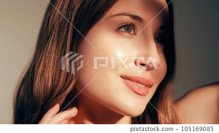 Beauty care. Radiant face. Moisturized skin. Cosmetology treatment. Pretty smiling young fresh glowing woman with glossy lip makeup enjoying sunshine isolated on beige. 105169085