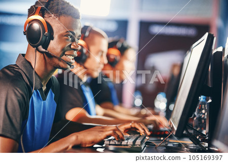 Side view of a young excited african guy, male cybersport gamer wearing headphones playing online video games while participating with team in eSport tournament Side view of a young excited african guy, male cybersport gamer wearing headphones playing online video games while participating with team in eSport tournament 105169397