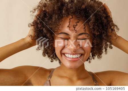 Beautiful lady with curly hairstyle posing against beige wall 105169405