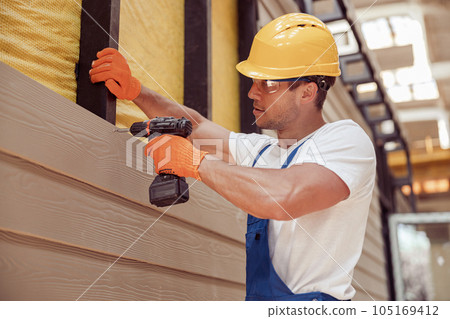 Male builder using power drill at construction site Male builder using power drill at construction site 105169412