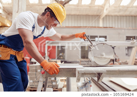 Joyful male worker using sawing machine in workshop 105169424
