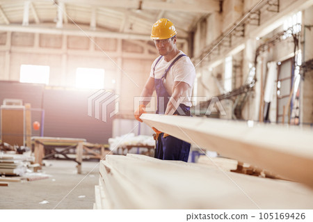Serious male builder carrying wooden plank at construction site Serious male builder carrying wooden plank at construction site 105169426