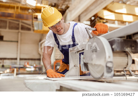 Smiling male worker using sawing machine in workshop Smiling male worker using sawing machine in workshop 105169427