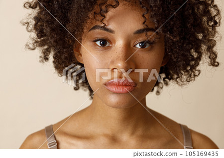 Beautiful lady with curly hairstyle posing against beige wall Beautiful lady with curly hairstyle posing against beige wall 105169435