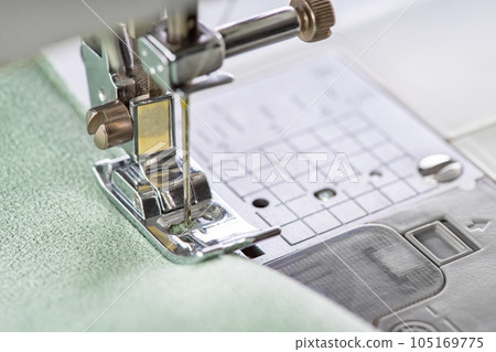 Modern sewing machine presser foot with green fabric and thread, closeup, macro 105169775