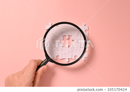Hand holding magnifying glass with white square puzzle pieces grid of business background, Jigsaw on background, Mock up on background with copy space for text or symbols, Background with copy space 105170424