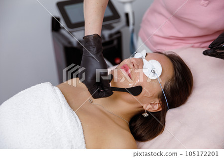 facial skin care, cosmetic facial procedure, rejuvenation procedure. doctor cosmetologist applies mask on woman's face in a beauty salon. cosmetologist performs facial treatments for a customer at an 105172201