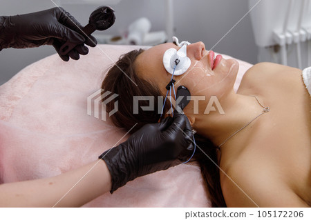 facial skin care, cosmetic facial procedure, rejuvenation procedure. doctor cosmetologist applies mask on woman's face in a beauty salon. cosmetologist performs facial treatments for a customer at an facial skin care, cosmetic facial procedure, rejuvenation procedure. doctor cosmetologist applies mask on woman's face in a beauty salon. cosmetologist performs facial treatments for a customer at an 105172206