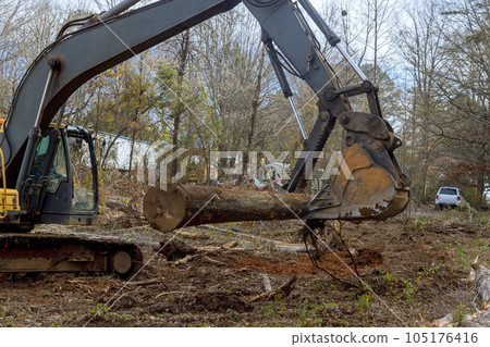 Worker is using an excavator to remove trees in forest a make way for house construction. Worker is using an excavator to remove trees in forest a make way for house construction. 105176416