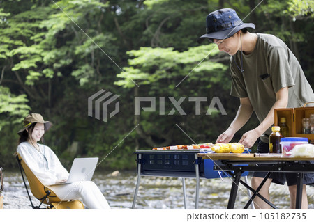 A man having a barbecue by the riverbed and a woman working on a computer A man having a barbecue by the riverbed and a woman working on a computer 105182735