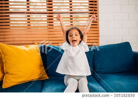 Happy cute girl with hands up sitting on comfortable sofa 105182850