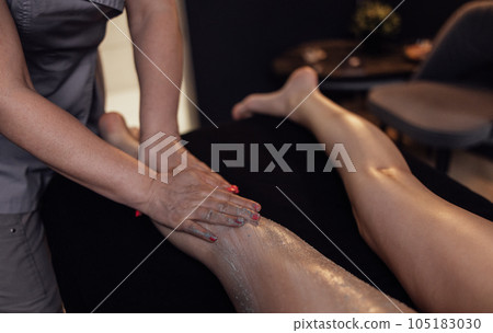 mMasseuse hands applying moisturizing scrab to the female client leg mMasseuse hands applying moisturizing scrab to the female client leg 105183030