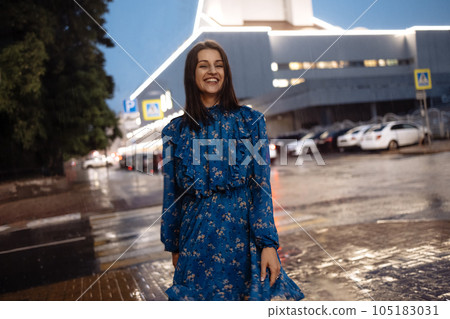 Beautiful brunette girl in blue dress laughs and dances in pouring rain in evening Beautiful brunette girl in blue dress laughs and dances in pouring rain in evening 105183031