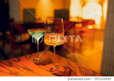 Two delicious ice cold cocktails in exquisite glasses stand on a wooden table in a restaurant. 105183095
