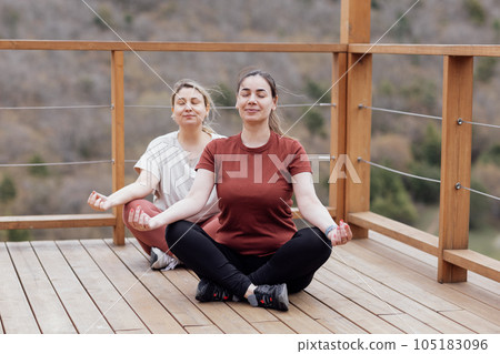 Two young women training asana yoga in park. Smiling girls are sitting in lotus position. Two young women training asana yoga in park. Smiling girls are sitting in lotus position. 105183096