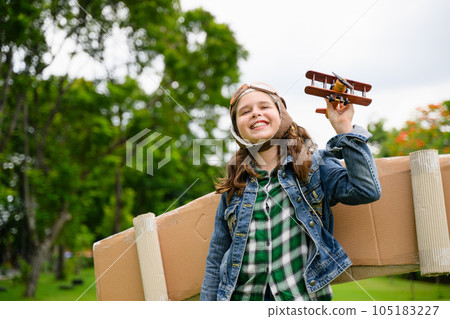 Happy girl playing with cardboard toy airplane handicraft in garden Happy girl playing with cardboard toy airplane handicraft in garden 105183227