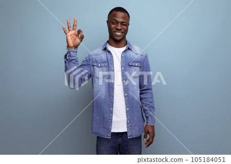 handsome young american man in denim jacket greets smiling on blue background with copy space handsome young american man in denim jacket greets smiling on blue background with copy space 105184051