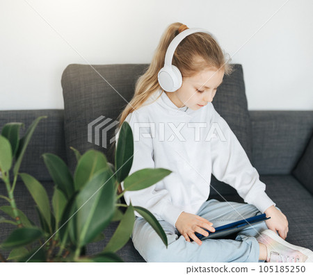 Little girl with headphones and tablet at home Little girl with headphones and tablet at home 105185250