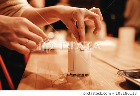 Master class of making candles. Closeup of beautiful female hands decorating candle with small shiny pebbles. 105186118