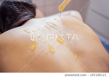 The masseur applies honey from a glass plate with a wooden stick on the back of his female client The masseur applies honey from a glass plate with a wooden stick on the back of his female client 105186121