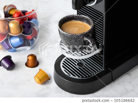 Black coffee cup and home espresso machine with coffee capsules on white marble kitchen. 105186682