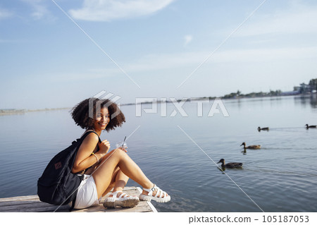 Beautiful mixed race female teenager sits on wooden pier Beautiful mixed race female teenager sits on wooden pier 105187053