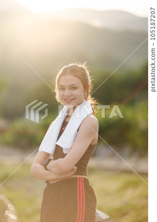 Portrait young attractive smiling fit woman with white towel resting after workout exercises outdoors on a background of park trees. Healthy lifestyle wellness happiness concept. Portrait young attractive smiling fit woman with white towel resting after workout exercises outdoors on a background of park trees. Healthy lifestyle wellness happiness concept. 105187207