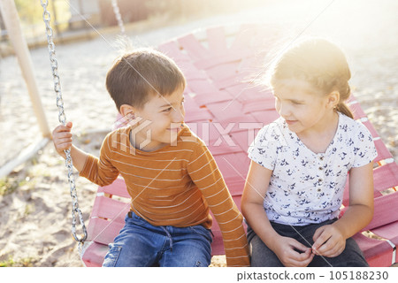 Cute little children ride on a pink wicker swing. Cheerful boy and girl are smiling at each other. 105188230