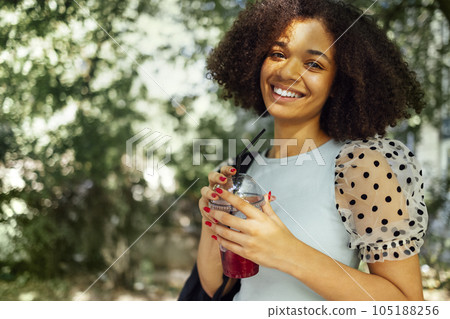 Smiling darkskin female teenager walking with iced cocktail in her hands 105188256