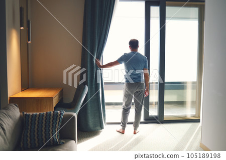Young man in casual clothes opens curtain window in early morning. 105189198