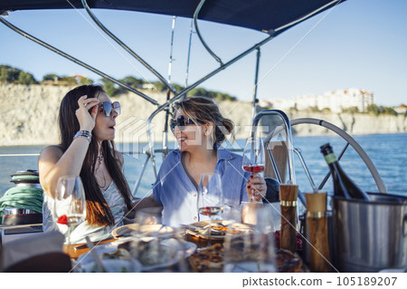 Two attractive women in sunglasses and casual clothes are having lunch on deck of ship. Two attractive women in sunglasses and casual clothes are having lunch on deck of ship. 105189207