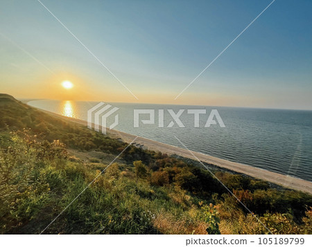 Beautiful landscape with sunset and sea. Sandy beach line with boats on the shore. Grass and bushes in the foreground. Wide angle. Sunshine glare. Peace and relaxation concept. Beautiful landscape with sunset and sea. Sandy beach line with boats on the shore. Grass and bushes in the foreground. Wide angle. Sunshine glare. Peace and relaxation concept. 105189799