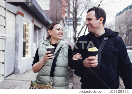 Young laughing couple walks through the city with takeaway coffee in their hands. 105189831