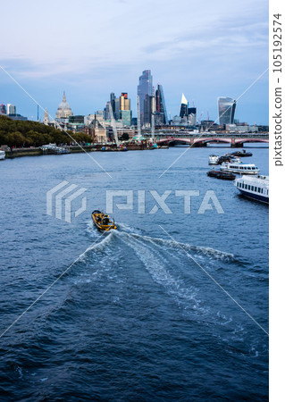 The streets of London at twilight: the River Thames flowing between skyscrapers and various ships coming and going The streets of London at twilight: the River Thames flowing between skyscrapers and various ships coming and going 105192574
