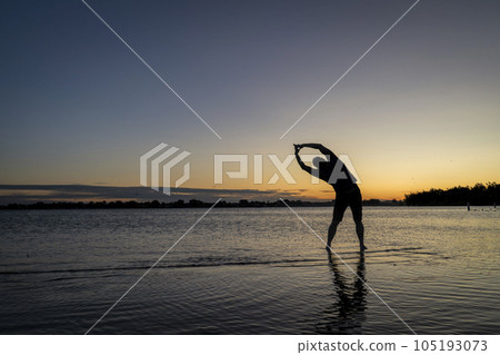 practicing yoga palm tree pose - sunrise silhouette of a man on a lake beach, Boyd Lake State Park in northern Colorado 105193073