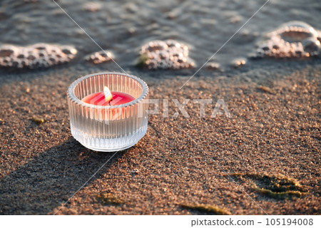 Burning candle lying on the sand near the water. Candles on the beach, combined with the sounds of the surf, create an atmosphere of a sea fairy tale and mystery. Burning candle lying on the sand near the water. Candles on the beach, combined with the sounds of the surf, create an atmosphere of a sea fairy tale and mystery. 105194008