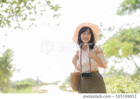 Portrait of asian young woman traveler with weaving hat and basket and a camera on green public park nature background. Journey trip lifestyle, world travel explorer or Asia summer tourism concept. 105199051